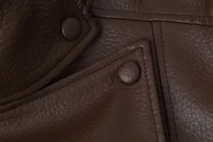 Close-up detail of dark brown faux leather motorcycle jacket with litchi texture and buttons