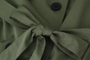 Close-up detail of olive green trench coat showing textured fabric and tied waist belt