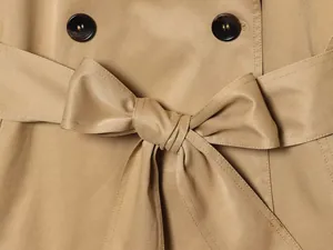 Primer plano de un cinturón de gabardina caqui anudado con un lazo y botones elegantes.