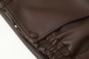 Detail shot of a brown faux leather biker jacket featuring a snap button and elastic hem