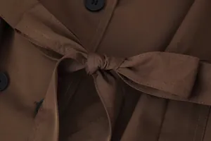 Macro detail view of a brown trench coat featuring a tied waist belt and black buttons.