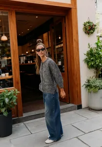 Female model in a grey marl knit cardigan and wide-leg jeans outside a cafe