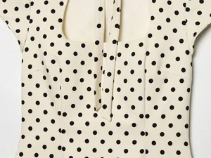 Vue détaillée d'une robe crème à pois noirs avec encolure carrée et détails de texture