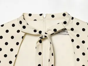 Détail du col d'une robe à pois crème avec un nœud papillon élégant et une fermeture éclair.