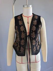 Gros plan d'un gilet vintage en daim noir orné de broderies dorées et de clous métalliques.