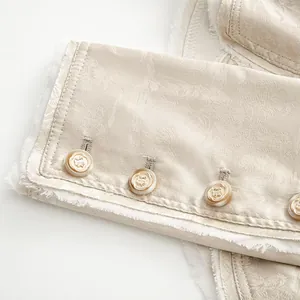 Nahaufnahme eines Jacquard-Blazer-Ärmels mit verzierten Goldknöpfen und Fransen.