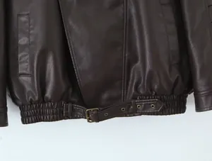Primer plano detallado de una chaqueta de cuero marrón vintage con hebilla de latón al borde.