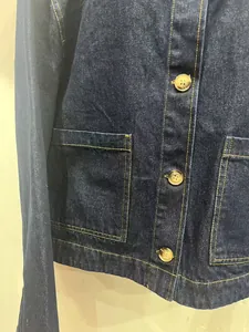 Detail van donkerblauw denim jack met twill-textuur, gouden stiksels en bruine knopen.