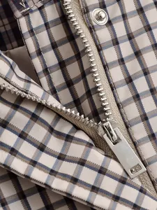 Gros plan sur la fermeture éclair en métal et le bouton d'une veste vintage à carreaux