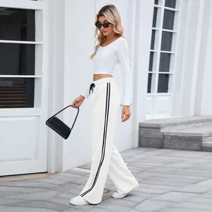 Femme en pantalon de jogging blanc à larges jambes et bandes noires dans un cadre urbain