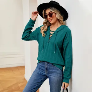 Detalle de sudadera con capucha verde azulado con cordones en el cuello y tejido texturizado.