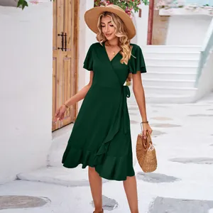 Detail view of dark green wrap V-neck dress with irregular ruffle hem in outdoor setting