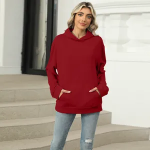 Full view of a model in a red oversized hoodie with front pocket on architectural stairs.