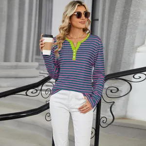 Woman styling a pink and teal striped long sleeve V-neck top in an urban street setting