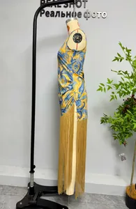 Side view of sleeveless paisley print dress featuring long golden fringe tassels.