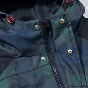 Macro shot of a green plaid windbreaker featuring a zipper and metal snap buttons.