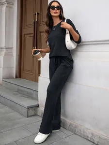 Stylish woman wearing a black ribbed knit lounge set while leaning against a white building wall