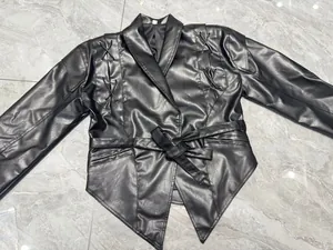 Flachbildansicht einer schwarzen Biker-Lederjacke mit Schnürung und Taillengürtel.
