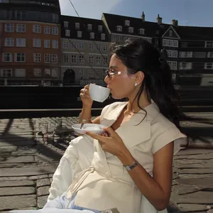 Zijaanzicht van vrouw in elegant crème mouwloos vest genietend van koffie buiten