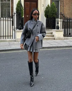 Détail street style d'un manteau court en laine gris à double boutonnage et jupe plissée