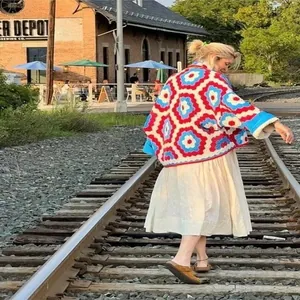 Detailed view of colorful floral crochet kimono jacket worn by model on railway tracks.