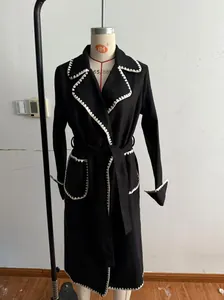 Détail d'un manteau en laine noir avec ceinture et bordure festonnée blanche unique.