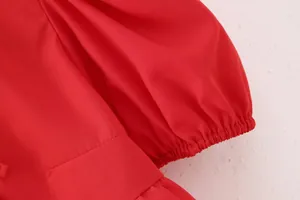 Gros plan du poignet élastique d'une chemise rouge à manches bouffantes en tissu texturé.