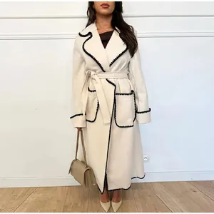 Détail d'un manteau en laine blanc avec des bords festonnés noirs et une ceinture
