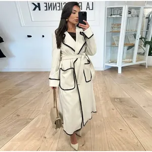 Manteau élégant en laine crème avec bordures noires contrastées et ceinture nouée.