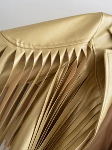 Detail macro view of golden metallic faux leather jacket showing long fringe tassels.