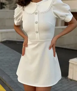 Detailed view of white mini dress featuring lace Peter Pan collar and jewel buttons.