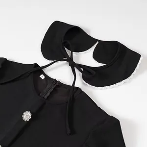 Detail view of a black dress with a detachable lace-trimmed collar and crystal button