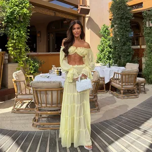 Model wearing light yellow off-the-shoulder crop top and tiered maxi skirt set in patio