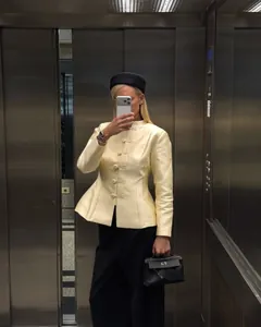 Woman in pale yellow Chinese style blazer with frog buttons during a mirror selfie session.