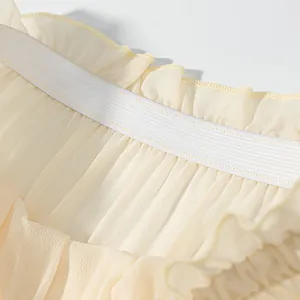 Close-up of flexible elastic waistband and layered cream chiffon ruffles detail.