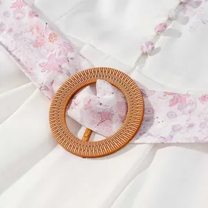 Detalle de un vestido de verano blanco con fajín de flores rosas y hebilla tejida redonda