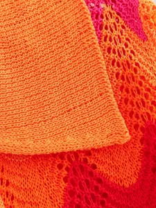 Détail macro de la maille tricotée orange vif et magenta montrant une texture complexe.