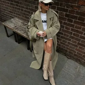 Full view of a stylish sage green wool coat with large lapels on a model sitting outdoors.