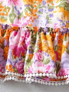 Nahaufnahme eines floralen Sommerkleides mit Rüschensaum und weißen Pompons-Details