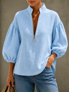 Detail van de lichtblauwe blouse met metalen rits, V-hals en lantaarnmouwen met textuur