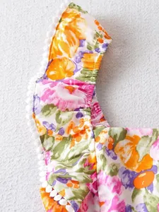 Nahaufnahme eines sommerlichen Blumenkleides mit Rüschen und weißem Pompon-Besatz.