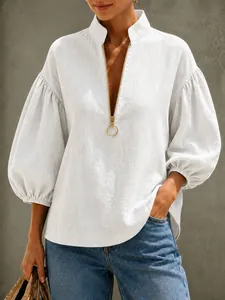Detailweergave van witte blouse met V-hals, gouden rits en gepofte lantaarnmouwen