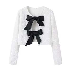 Detail view of a white sequined cropped jacket featuring two large black satin bows on the front.