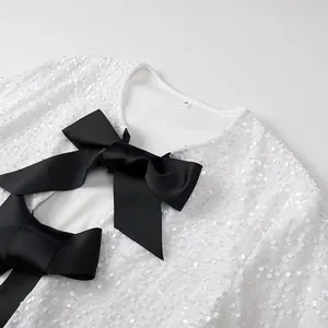 Close-up detail of a white sequin jacket featuring elegant large black grosgrain bows