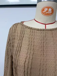 Détail montrant le tissu en maille jacquard texturé complexe d'une robe marron à col rond