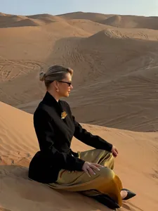 Model wearing elegant black mermaid hem blazer and gold satin pants in desert sunset