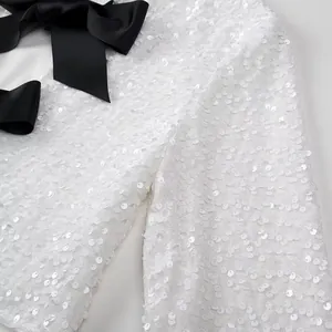 Macro view of white sequin texture and black satin bow on an elegant women's top.
