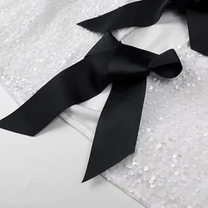 Close-up detail of white sequin top featuring a large black grosgrain ribbon bow