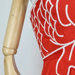 Close-up of exquisite white goldfish scale embroidery on a vibrant red cotton dress.