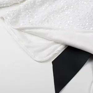 Close-up of white sequined fabric with elegant black ribbon bow detail.